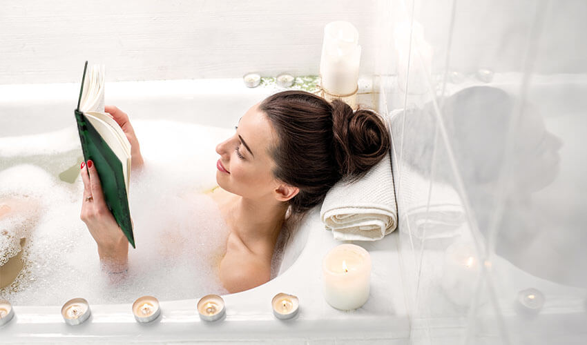 Woman relaxing in a bath reading a book